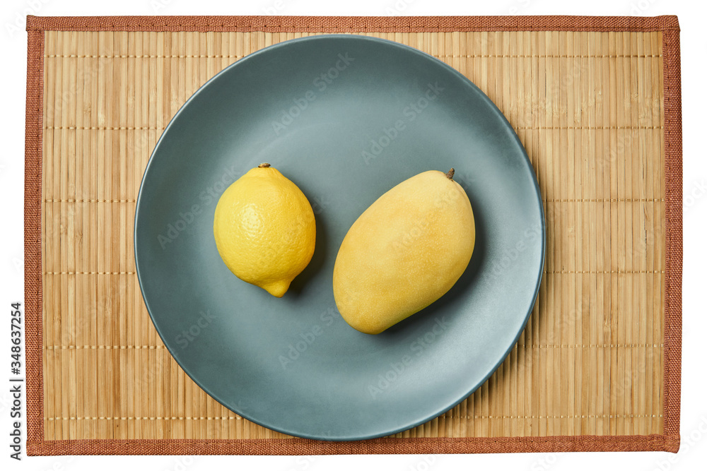 Wall mural bright lemon and yellow mango on a gray plate on a cane tablecloth