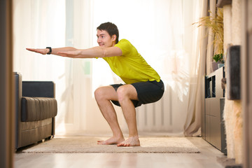 Man in t-shirt and shorts is doing squat exercises at home.