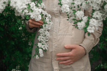 pregnant woman outdoors hugging her stomach on the background of flowers 