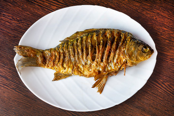 Grilled crucian carp on a white plate on a rustic table. River fish, organic food. Top view. Close-up