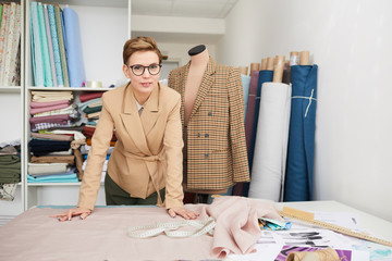 Portrait of young fashion designer in eyeglasses looking at camera while standing near her...