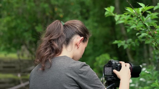 A young girl, a photographer, takes pictures of beautiful nature in a forest area where a stream flows.