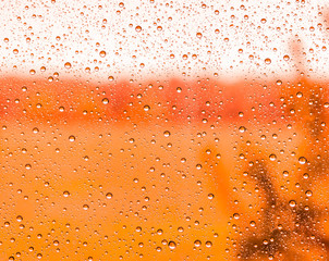 red rain water drops on a window glass close up , colored drop macro in a orange light ; ginger textute background