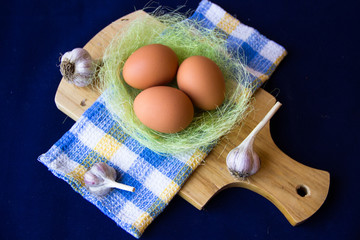 Chicken eggs. Brown chicken eggs in basket on the cutting board on blue background. Copy space. Still life with eggs and garlic. Farm natural products. Egg and vegetables is ingredient for cooking