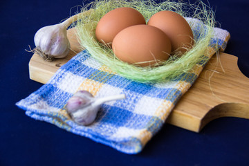 Chicken eggs. Brown chicken eggs in basket on the cutting board on blue background. Copy space. Still life with eggs and garlic. Farm natural products. Egg and vegetables is ingredient for cooking