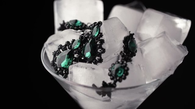 Glass goblet with ice cubes and precious jewelry. Time lapse ice is melting. Close up of an emerald bracelet with ice cubes. Concept for sales and price cuts.
