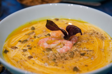Tasty pumpkin cream soup with shrimps and basil leaves