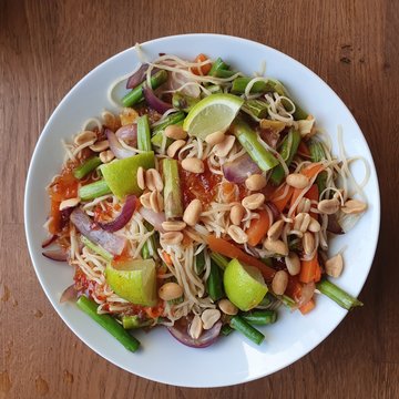 Wok dish nuddles with veggies peanuts and lime. white bowl on wood table, shot from above. food healthy