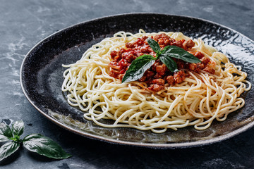 Italian pasta with meat tomato sauce and Basil on a black plate close up