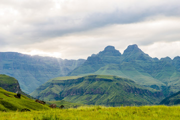 Fototapeta na wymiar Südafrika, KwaZulu-Natal, Giants Castle Game Reserve, Cathedral Peak in den Drakensbergen, Grüne Berglandschaft unter grauer Wolkendecke