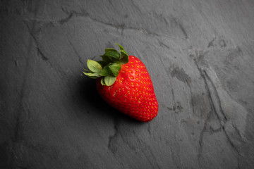 A strawberry on a black stone background, dark food photography