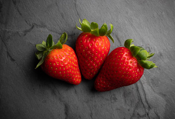 three strawberries on a black stone background, dark food photography
