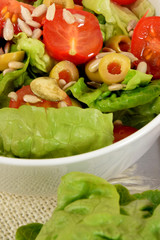 green lettuce with tomatoes, green olives and sunflower seeds in a white bowl