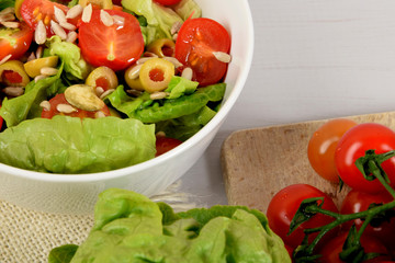 green lettuce with tomatoes, green olives and sunflower seeds in a white bowl