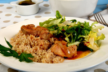 A piece of meat on cooked barley and green lettuce with additions