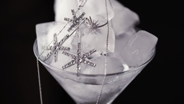 Glass goblet with ice cubes and precious jewelry. Time lapse ice is melting. Close up of silver earrings and chain with ice cubes. Concept for sales and price cuts.