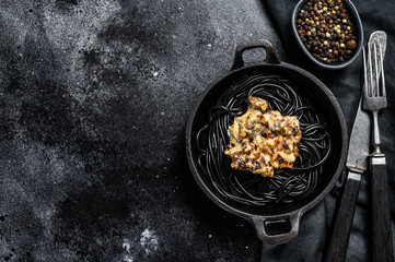 Black spaghetti pasta with squid ink in a pan. Beef in pepper sauce. Black background. Top view. Copy space