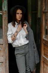 Beautiful young  pensive girl with long hair, wears a stylish hat, a gray coat, a white shirt and pants, poses for an outdoor portrait in daylight, showing a female spring and autumn fashion concept.