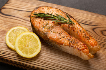 Grilled salmon steak with lemon on dark background, fried salmon fillet on wooden board, close up.