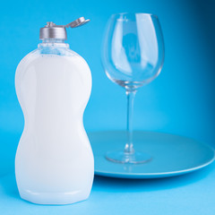Clean washed dishes on blue background. Concept of washing dishes. Dishwashing liquid and plates with wine glasses.