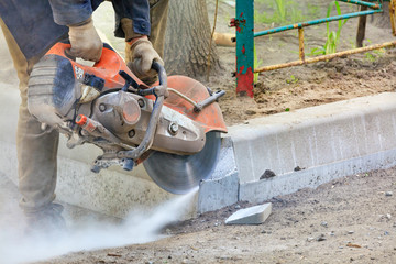 Worker at a construction site using a concrete saw cuts concrete curbs. © Sergii
