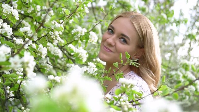 Beauty young woman enjoying nature in spring apple orchard, Happy Beautiful girl in Garden with blooming trees. Portrait of Beautiful blonde girl posing in blooming tree branches with white flowers 4k
