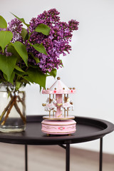 Pink Musical carousel and Bouquet of beautiful spring lilac flowers in vase on vintage coffee table, on an isolated white background. Closeup vintage musical carousel toy with pink and white horses.  