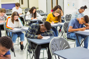 Focused high school students taking exam at desks in classroom