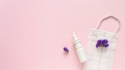 Obraz na płótnie Canvas Seasonal spring summer allergy flowers concept. White spray container with purple flowers and medical protective mask on pink background. Creative flat lay composition, copy space