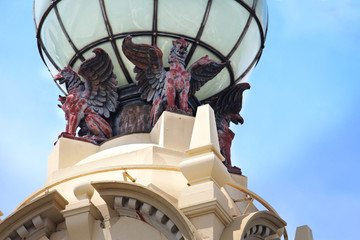 Architectural feature of a historic retail building. Winged Griffins holding up a white globe. The...