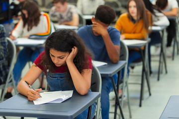 Focused high school girl student taking exam at desk in classroom