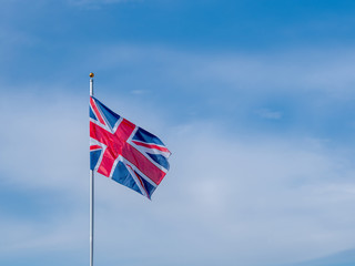 Great Britain Union Jack flag flying on a flagpole in breeze with blue sky and copy space.