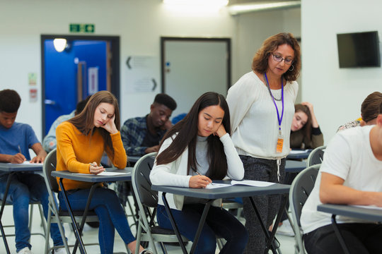 High school teacher supervising students taking exam at desks
