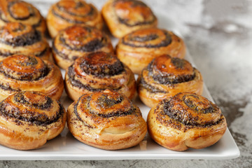 Freshly baked sweet buns rolls with poppy seeds on a white plate.