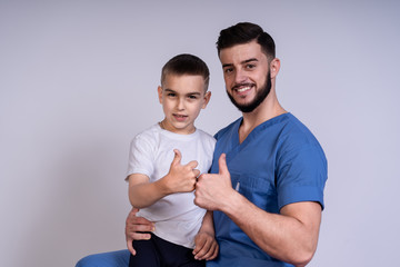 A little boy stands beside his doctor, and together they show a sign of class, concept of treatment and friendship