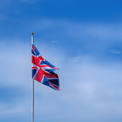 Great Britain Union Jack flag flying on a flagpole in breeze with blue sky and copy space.