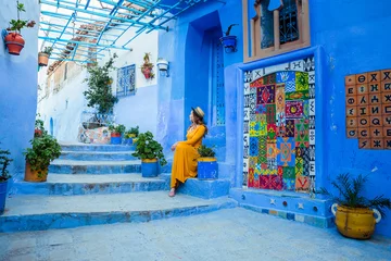 Keuken foto achterwand Beautiful caucasian woman in a yellow dress and a boater hat posing in a blue city in Morocco. Chefchaouen. © viktoriia1974