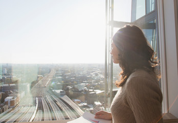 Thoughtful businesswoman at sunny window overlooking city