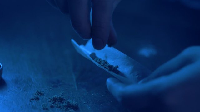Man rolling a medical marijuana joint in night club. Close up of addict marijuana joint with lighter. Drugs narcotic concept. Close up . Drug use. Man preparing and rolling marijuana cannabis joint.