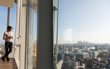 Businessman standing at sunny urban highrise office window