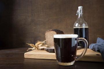 Russian kvass from rye bread in special half-liter mug with loaf bread on dark background. Fermented beverage. Copy space.