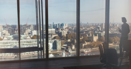 Silhouette businessman at highrise window overlooking city, London, UK