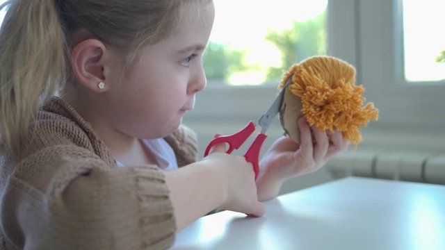 Concentrated little girl in process of making handmade pompom in morning kitchen