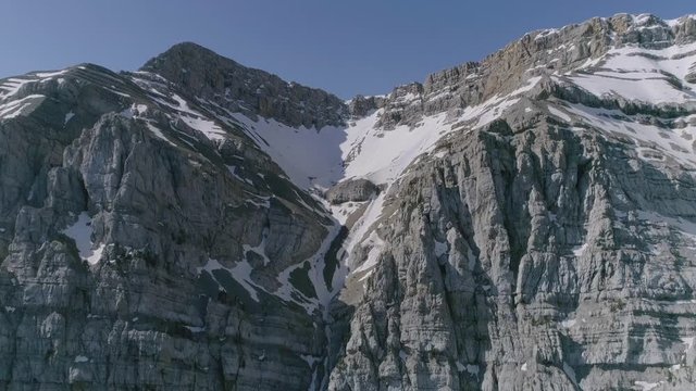 AERIAL DRON BACKWARD SHOT DISCOVERING STUNNING HUGE MOUNTAIN RANGE IN SPRING WITH SNOW AND GREEN FIR TREES