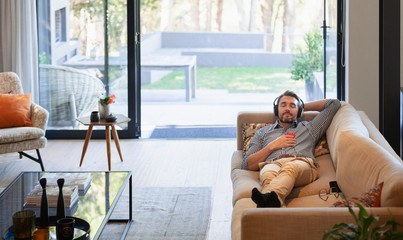 Man relaxing on living room sofa, listening to music with headphones and mp3 player