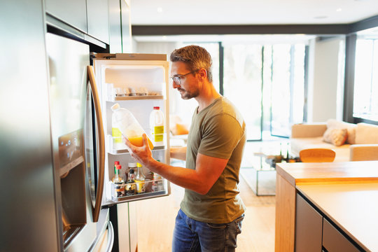 Man holding orange juice at open refrigerator in kitchen