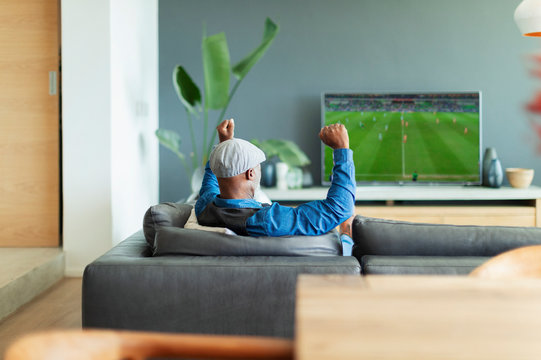 Excited man cheering, watching soccer match on TV in living room