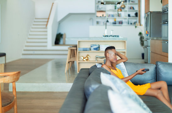 Young Woman With Remote Control Watching TV On Living Room Sofa