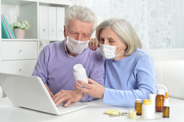 Fototapeta premium Ill senior couple with facial masks using laptop