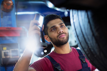 Focused male mechanic with flashlight examining tire in auto repair shop